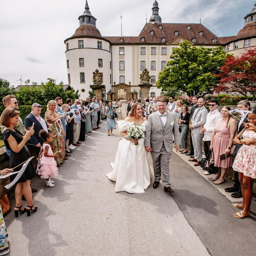 Auszug des Brautpaares nach einer zweisprachigen, freien Trauung auf einem Schloss. Die internationale Hochzeitsgesellschaft steht Spalier und feiert das Paar mit wehenden Wedding Wands vor der historischen Schlosskulisse.